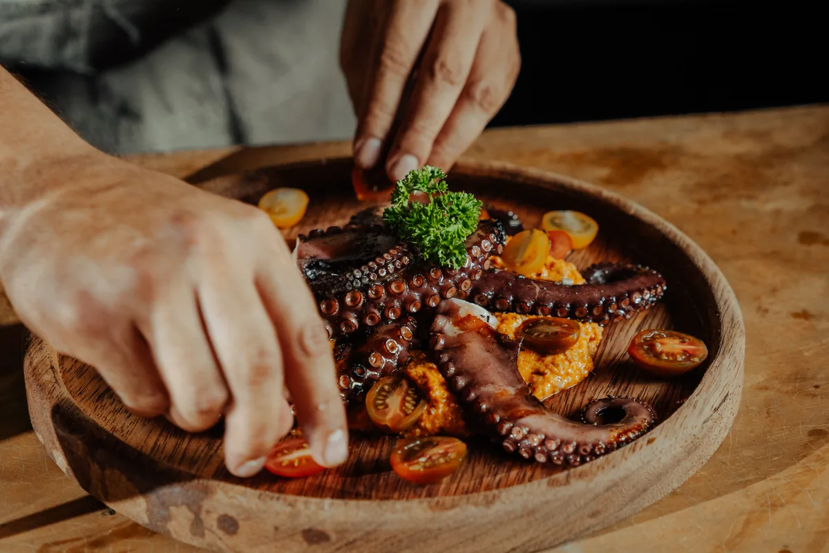 Chef Ubaldo Martínez finishing a course of grilled octopus on a wooden board