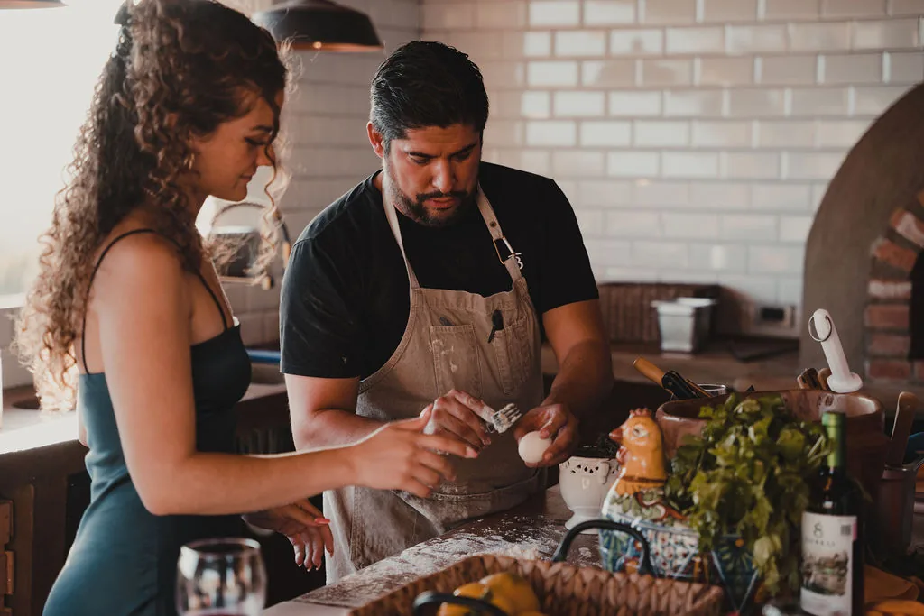 Chef teaching a guest to prepare a dish at the kitchen island over a glass of wine