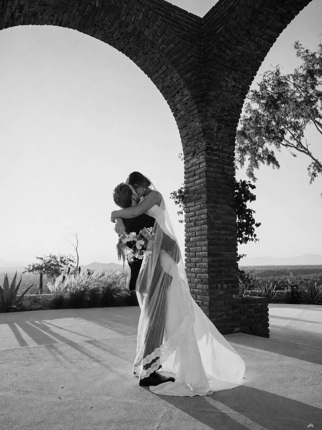 Bride and groom embracing beneath the brick arch of the estate