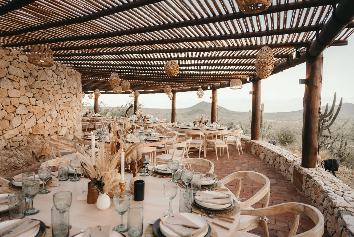 Tables set under the pergola between granite stone walls at sunset