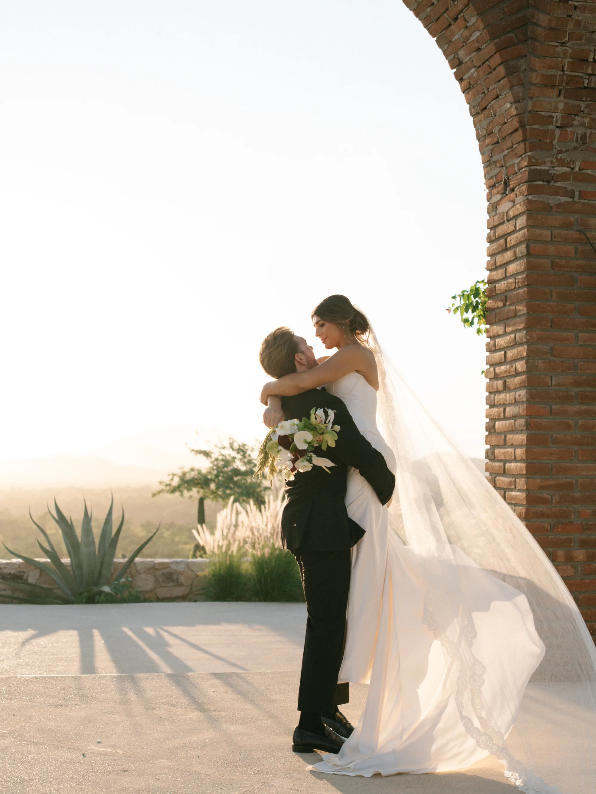 Bride and groom beneath the brick arch with the desert light behind them