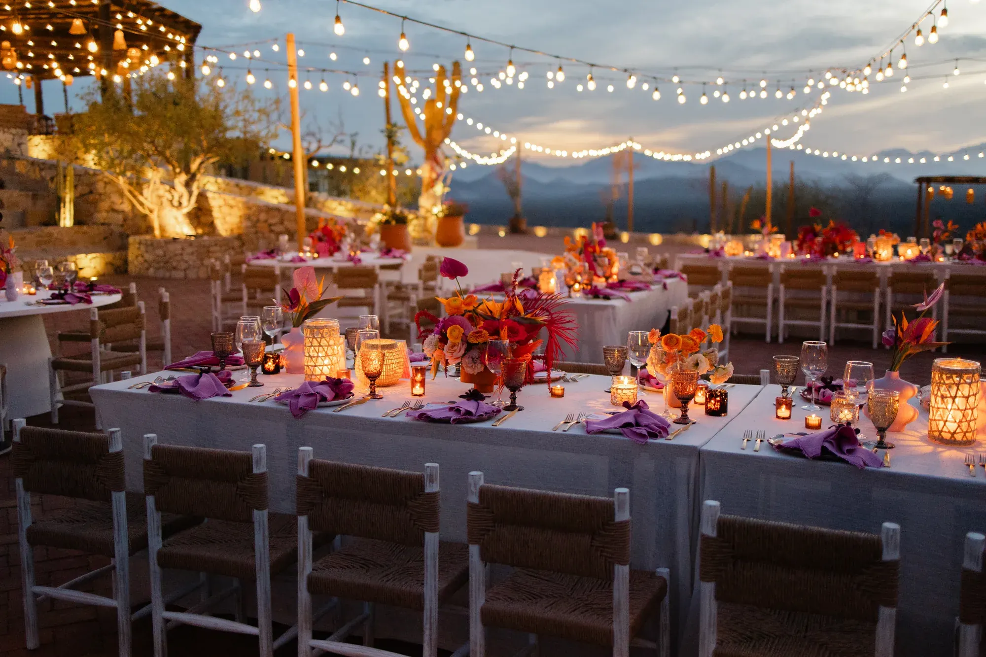 Reception tables in vivid florals under string lights at dusk
