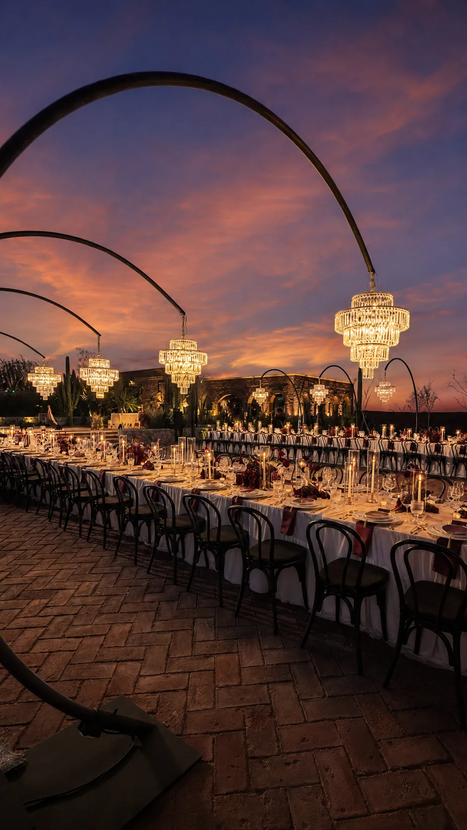 Long table beneath chandeliers on the brick patio at dusk