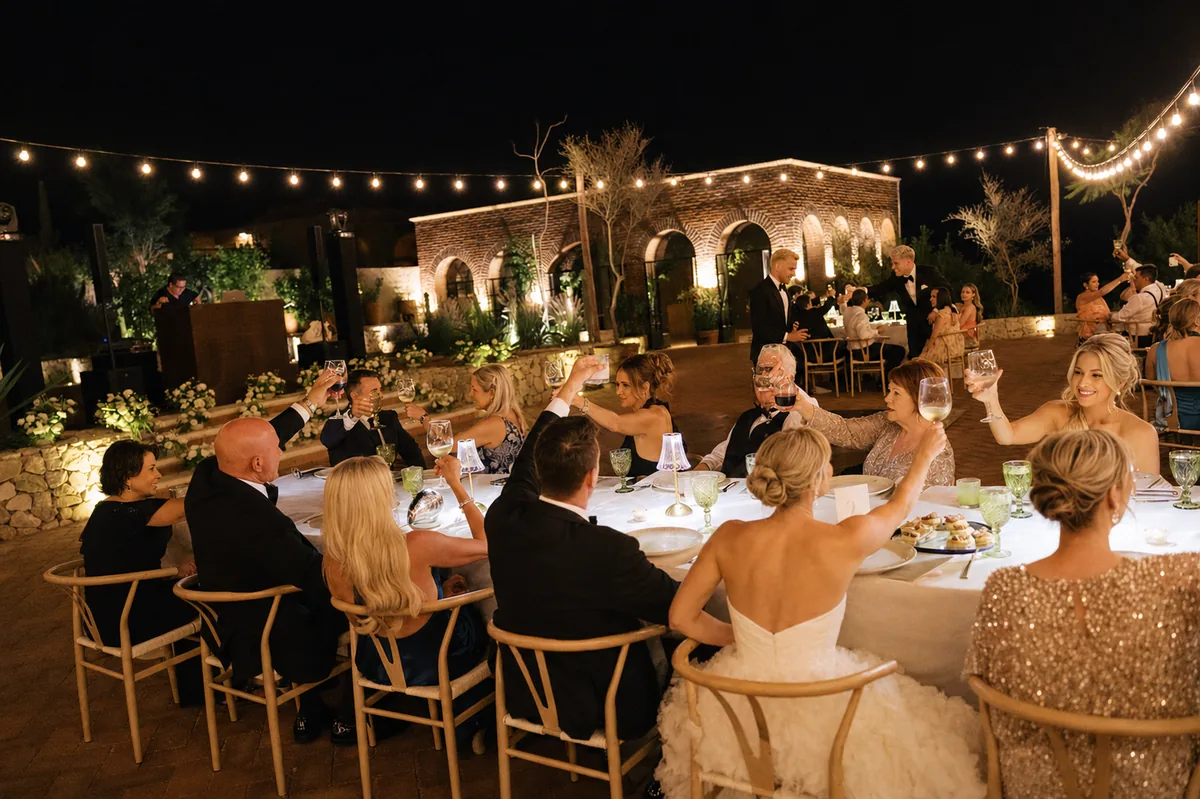 Guests raising a toast at a candlelit table with the estate lit behind them