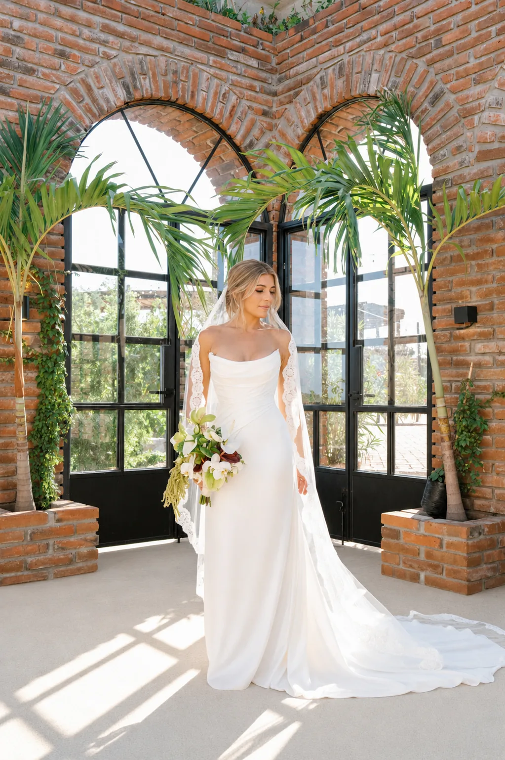 Bride standing in the greenhouse framed by brick arches and tall windows